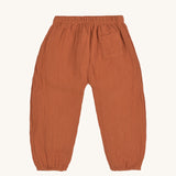 The back of the Lassig organic cotton muslin pants in an orange rust colour.