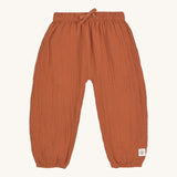 The Lassig organic cotton muslin baby pants in an orange rust colour.