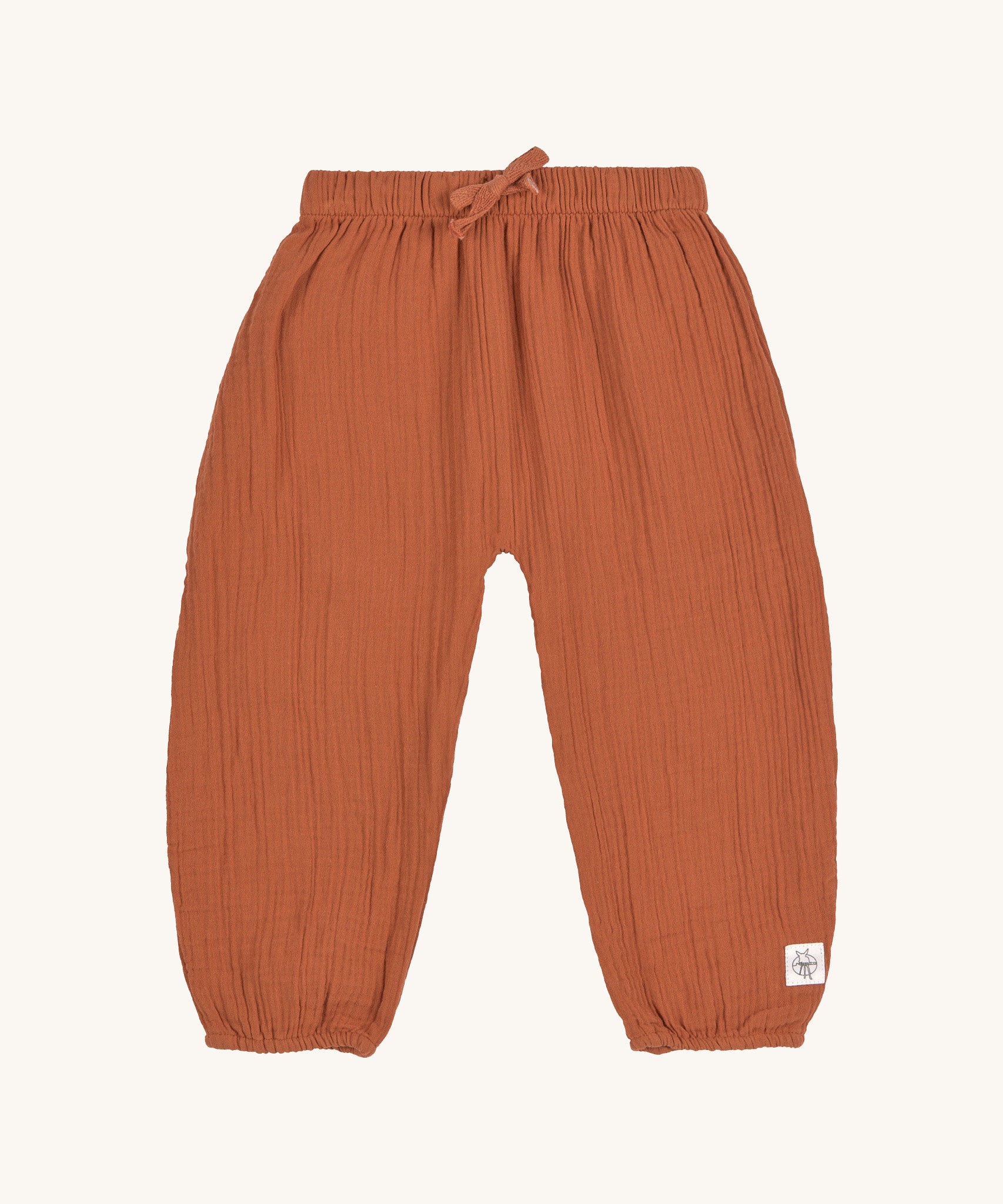 The Lassig organic cotton muslin baby pants in an orange rust colour.