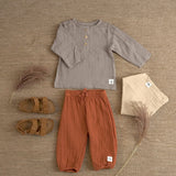 An organic cotton muslin outfit from Lassig, laid out on the floor. It includes the Lassig muslin pants in orange rust.