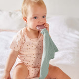 A baby chewing the Lassig rubber strawberry teether, attached to the organic cotton muslin baby comforter.