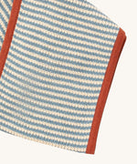 A close up of the Little Green Radicals knitted scarf in blue stripes. showing the blue and cream stripes detail on organic cotton fabric