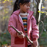 child wearing pink little green radicals coat holding a branch in a forest setting