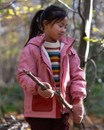 child wearing pink little green radicals coat holding a branch in a forest setting