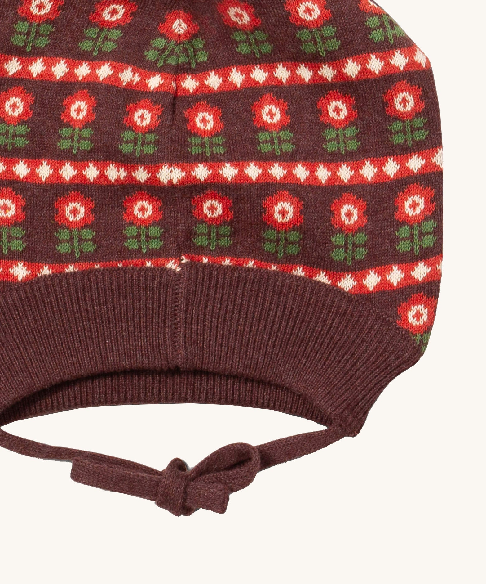 A close up of the Little Green Radicals flower collecting knitted beanie hat showing the closed dark orange tie detail on brown organic cotton fabric
