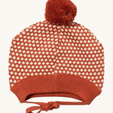 Little Green Radicals ginger diamond knitted beanie hat available at Babipur. A  knitted GOTS organic cotton beanie style hat with a dark orange and cream diamond design and light brown pom pom on top. Features matching dark orange ties for a secure fit.