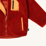 A close up of the Little Green Radicals zip up fleece jacket in ginger showing the chest pocket detail with light orange trim on dark orange fleece fabric.