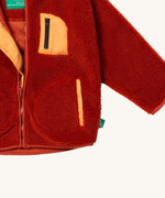 A close up of the Little Green Radicals zip up fleece jacket in ginger showing the chest pocket detail with light orange trim on dark orange fleece fabric.