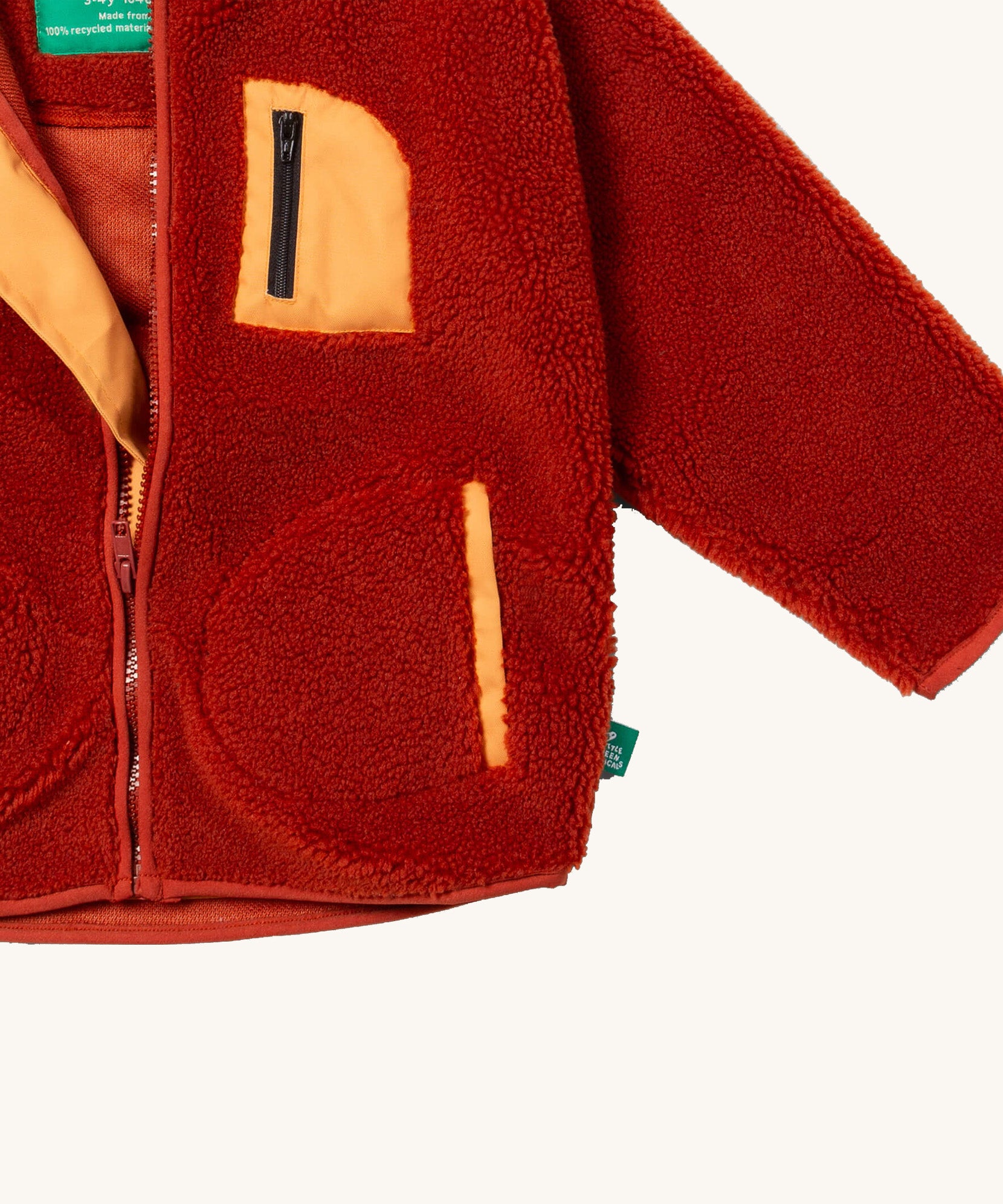 A close up of the Little Green Radicals zip up fleece jacket in ginger showing the chest pocket detail with light orange trim on dark orange fleece fabric.