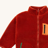 A close up of the Little Green Radicals zip up fleece jacket in ginger showing the chest pocket detail with light orange trim and side pocket on dark orange fleece fabric.