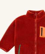 A close up of the Little Green Radicals zip up fleece jacket in ginger showing the chest pocket detail with light orange trim and side pocket on dark orange fleece fabric.