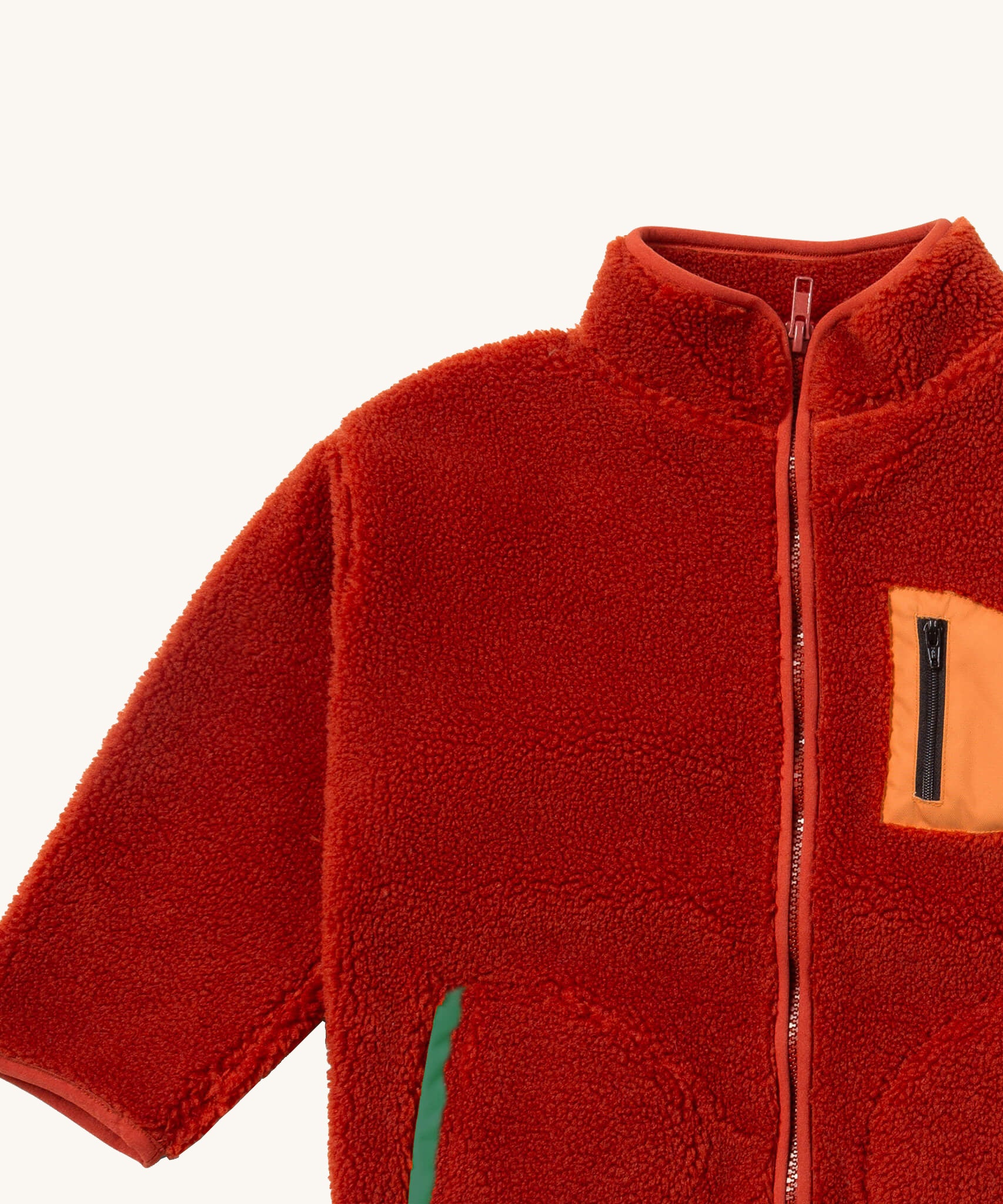A close up of the Little Green Radicals zip up fleece jacket in ginger showing the chest pocket detail with light orange trim and side pocket on dark orange fleece fabric.