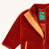 A close up of the Little Green Radicals zip up fleece jacket in ginger showing the full length zip detail with light orange trim on dark orange fleece fabric.