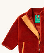 A close up of the Little Green Radicals zip up fleece jacket in ginger showing the full length zip detail with light orange trim on dark orange fleece fabric.