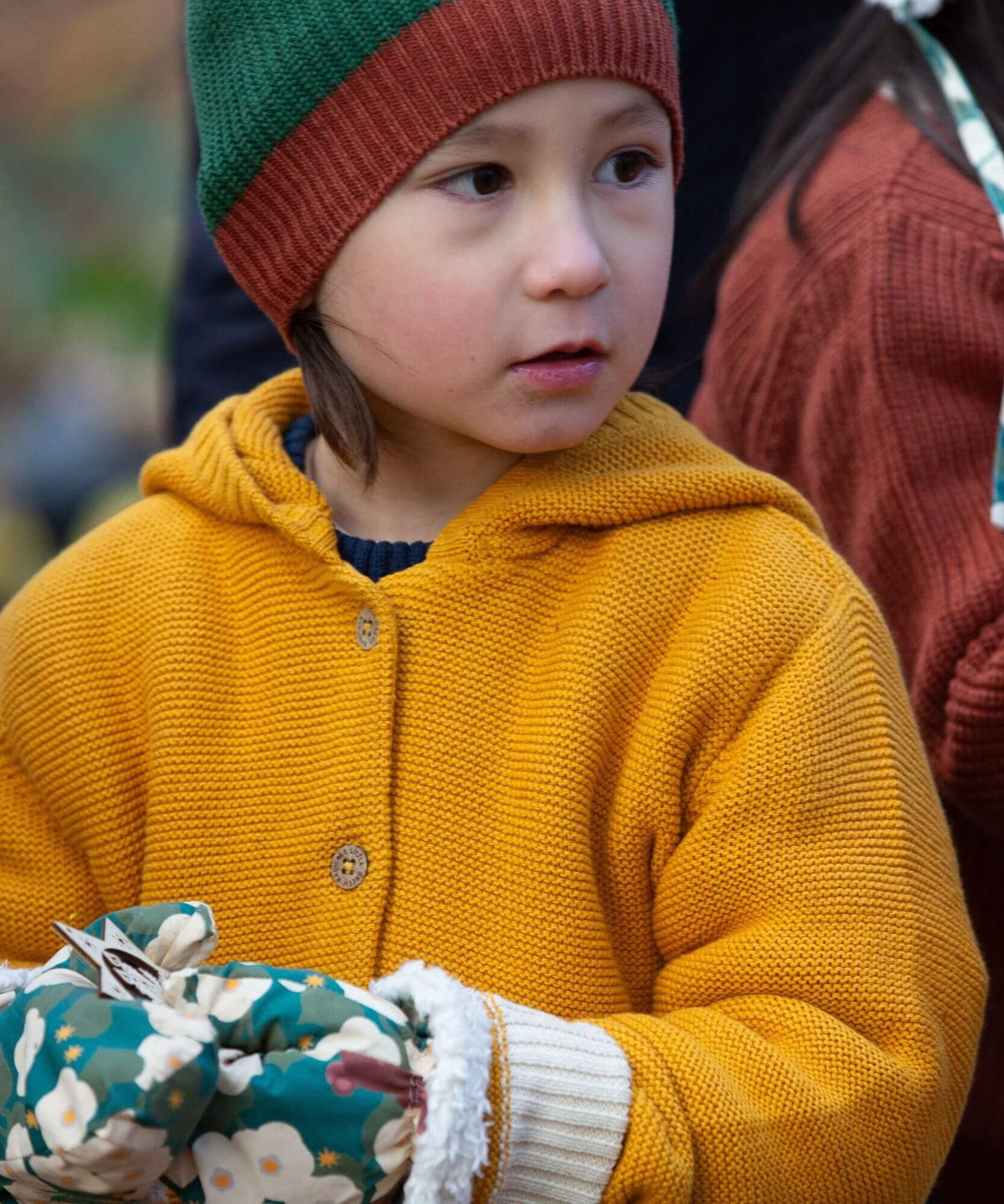 A close up of a child wearing the Little Green Radicals gold snuggly hooded knitted cardigan.Showing the knit detail on yellow organic cotton fabric.