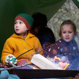 A child sitting under a shelter in woodland wearing the Little Green Radicals gold snuggly hooded knitted cardigan. A thick knitted cardigan with a generous hood for warmth and button fasteners  down the middle on yellow organic cotton fabric.