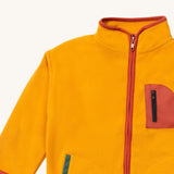 A close up of the Little Green Radicals polar fleece jacket in gold showing the red trim and full length zip detail on dark yellow recycled polyester fabric.