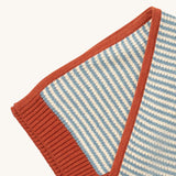 A close up of the Little Green Radicals knitted scarf in blue stripes. showing the blue and cream stripes and red trim detail on organic cotton fabric.