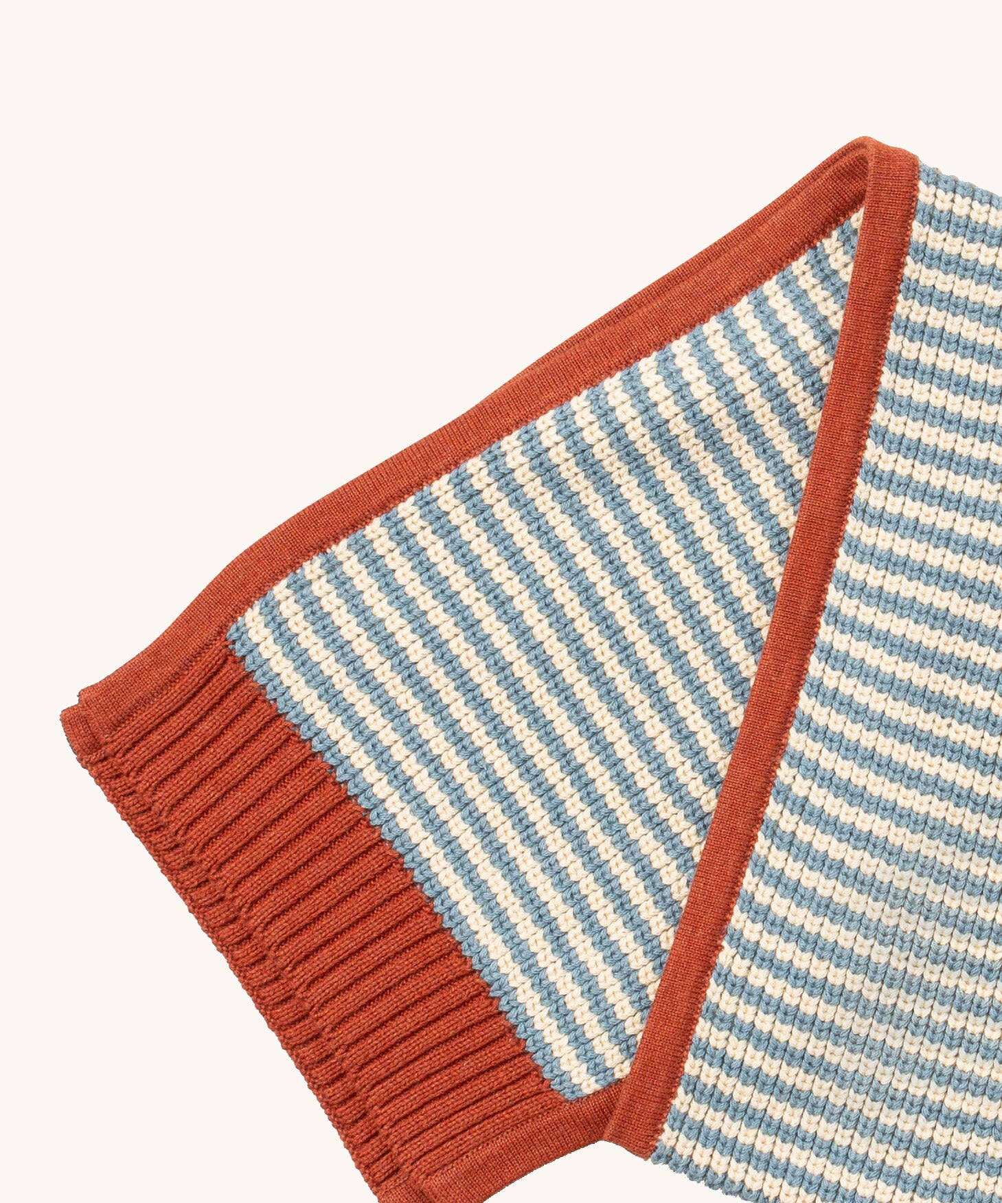 A close up of the Little Green Radicals knitted scarf in blue stripes. showing the blue and cream stripes and red trim detail on organic cotton fabric.