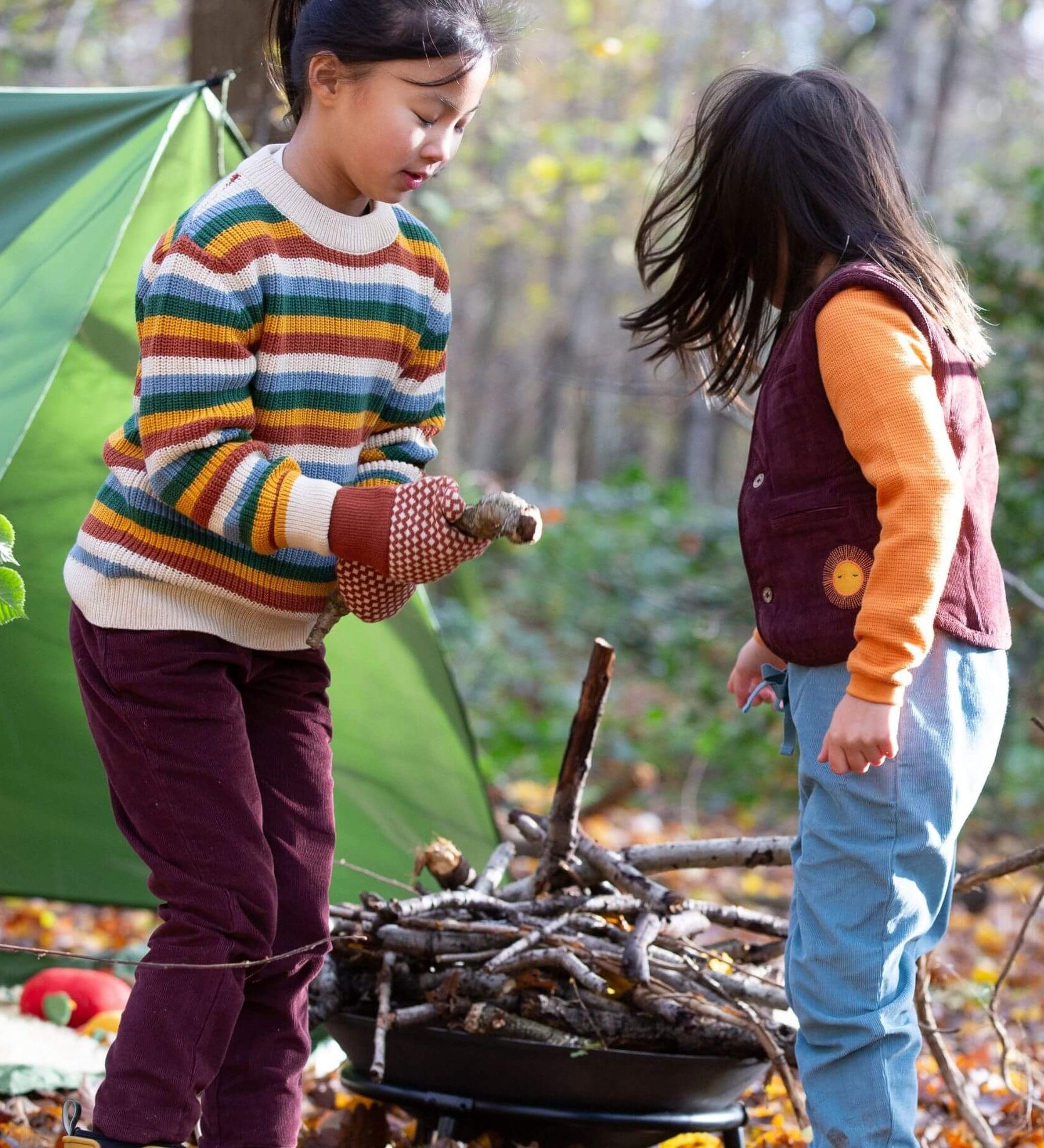 2 children playing with sticks in woodland wearing the Little Green Radicals comfy corduroy trousers in chocolate and pale blue
