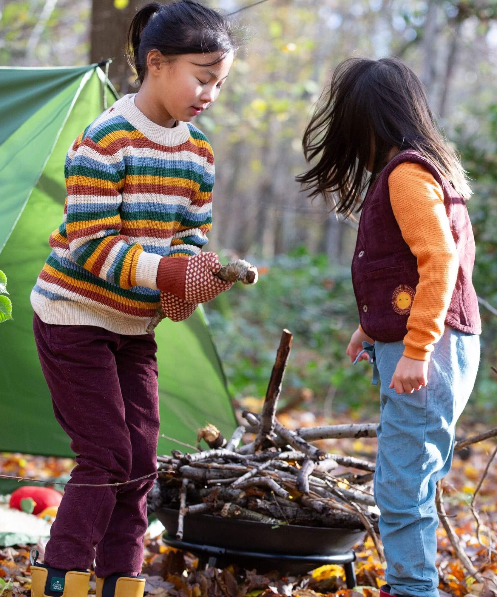 2 children playing with sticks in woodland wearing the Little Green Radicals comfy corduroy trousers in chocolate and pale blue