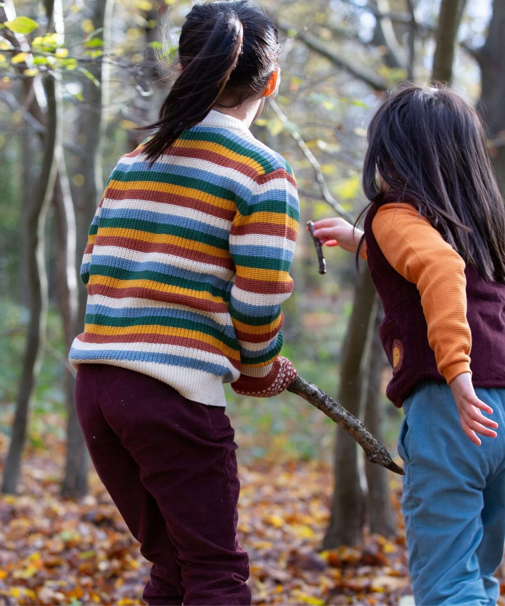 2 children playing with sticks in woodland wearing the Little Green Radicals comfy trousers in a corduroy style made from GOTS organic cotton.