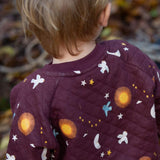 A close up of a child wearing the Little Green Radicals flying birds quilted sweatshirt that's available at Babipur. Showing the quilted detail and a close look at the lying birds print on dark maroon organic cotton fabric