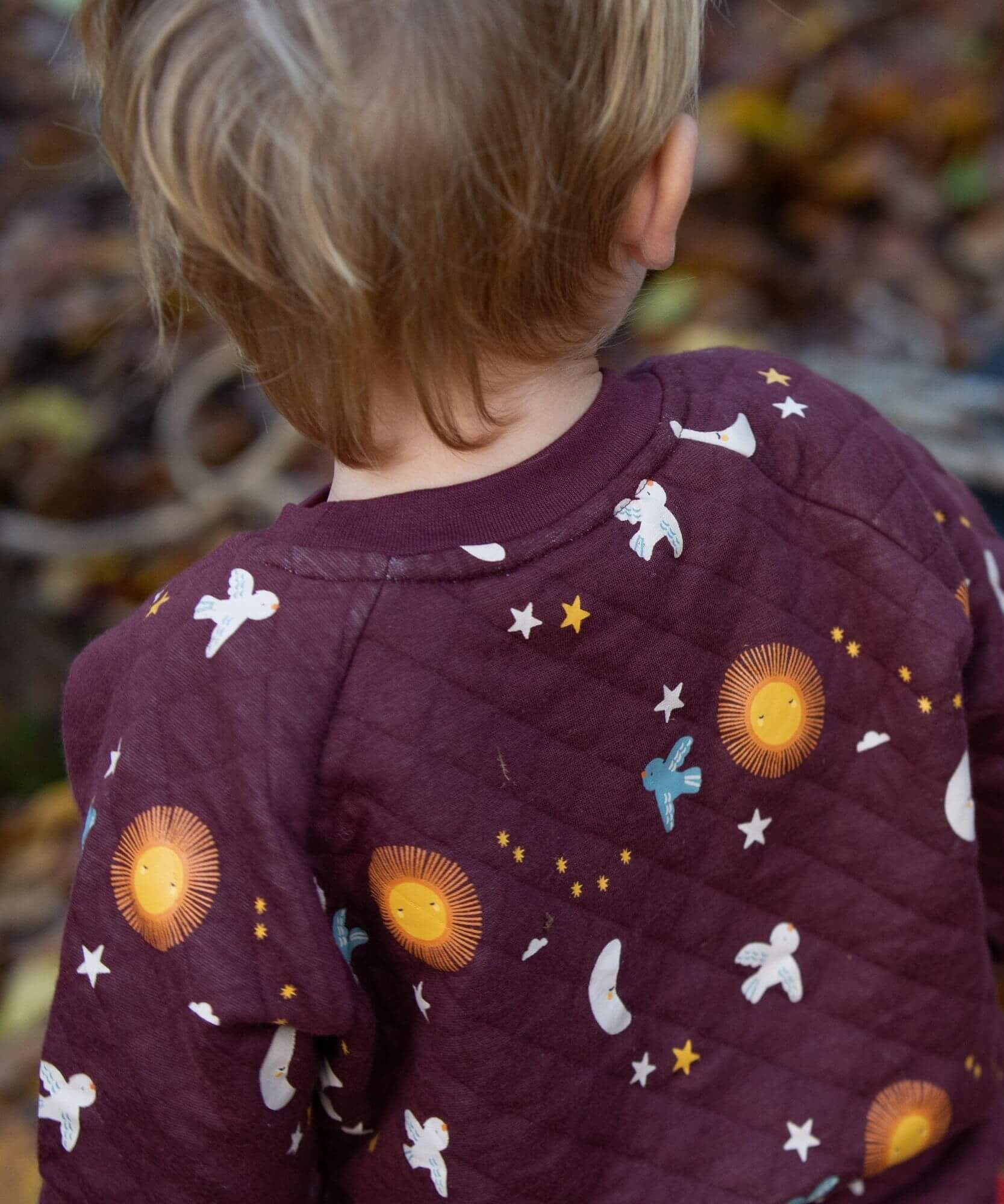 A close up of a child wearing the Little Green Radicals flying birds quilted sweatshirt that's available at Babipur. Showing the quilted detail and a close look at the lying birds print on dark maroon organic cotton fabric