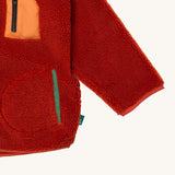 A close up of the Little Green Radicals zip up fleece jacket in ginger showing chest and side pocket detail on dark orange fleece fabric.