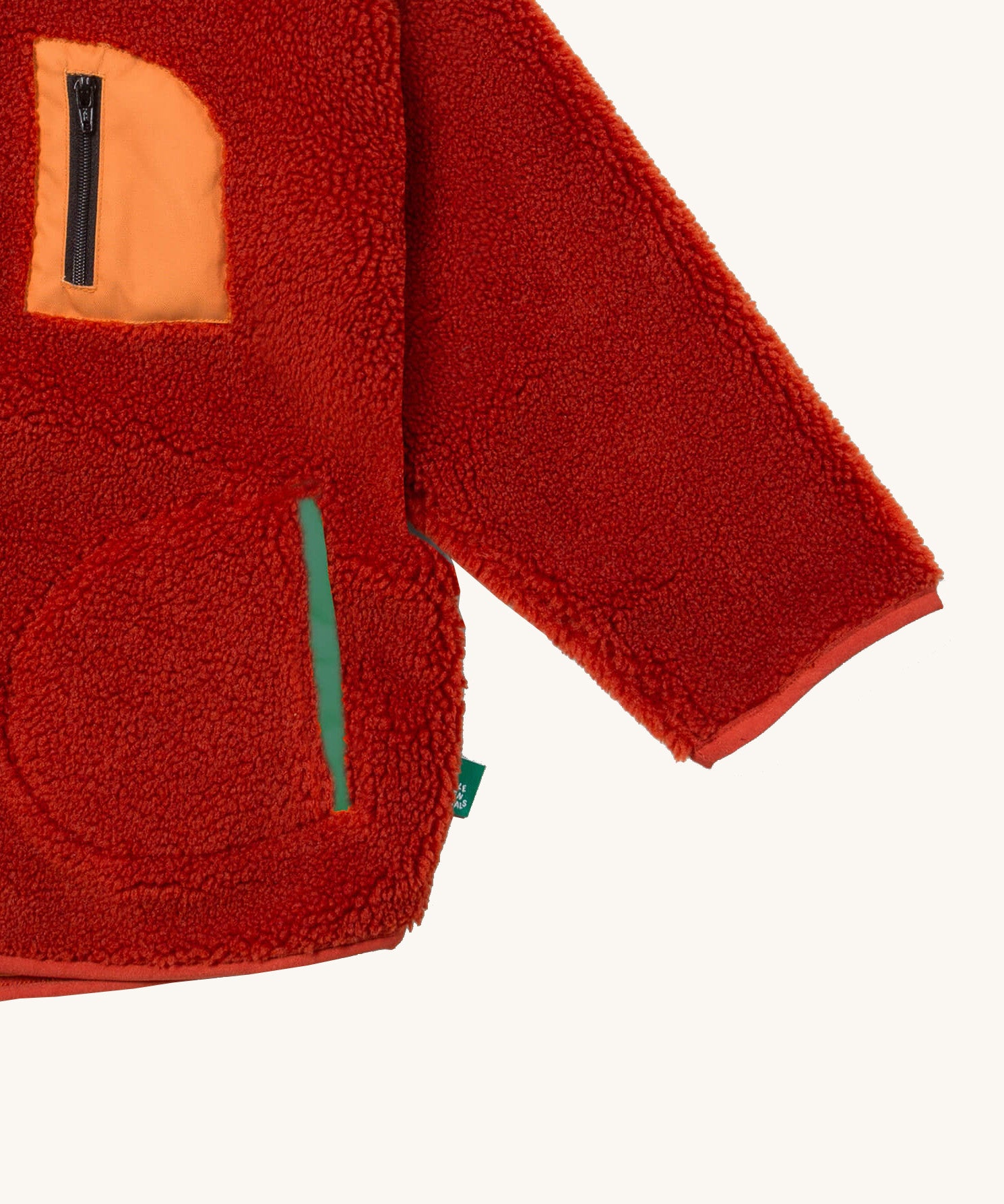 A close up of the Little Green Radicals zip up fleece jacket in ginger showing chest and side pocket detail on dark orange fleece fabric.