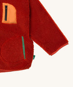 A close up of the Little Green Radicals zip up fleece jacket in ginger showing chest and side pocket detail on dark orange fleece fabric.