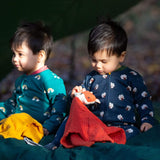A child sitting on the floor in the woods and wearing the Little Green radicals navy sheep baby grow and holding a fox comforter. A soft GOTS organic cotton all in one in navy with cute sheep prints