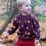 A child playing in woodland and wearing the Little Green Radicals flying birds quilted sweatshirt that's available at Babipur. A thick quilted sweatshirt with cute prints of birds flying through a starry night on dark maroon organic cotton fabric.