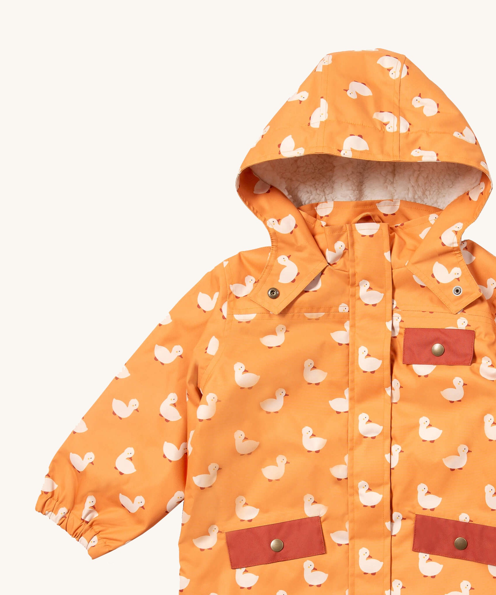 A close up of the Little Green Radicals waterproof adventure coat in gold ducks showing the sherpa fleece liner under the hood, the full length zip and 2 side pockets in red trim detail on yellow recycled polyester fabric