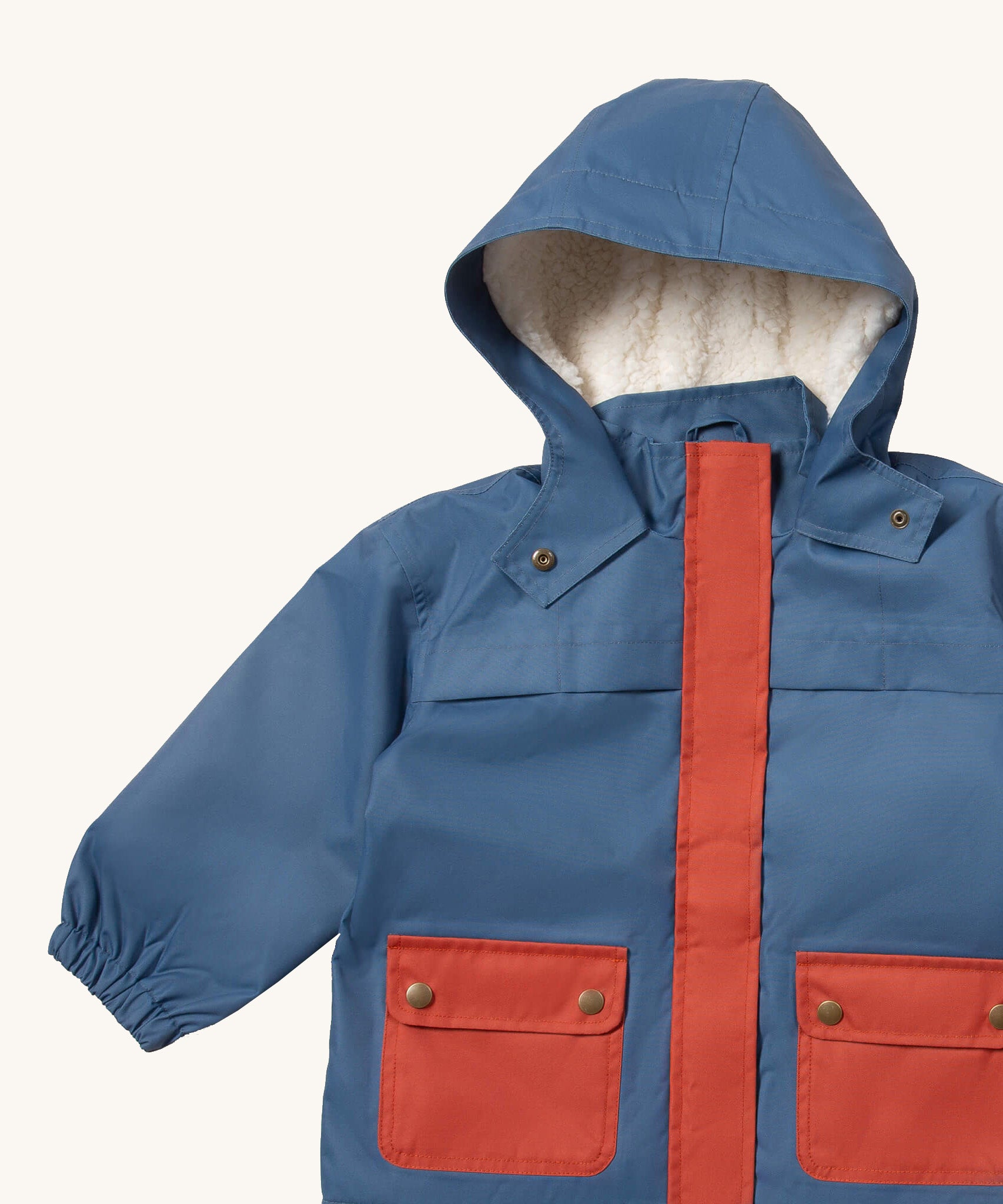 A close up of the Little Green Radicals waterproof coat in moonlight blue Showing the sherpa fleece liner, the full length zip and 2 side pockets in red trim detail on blue recycled polyester fabric