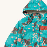 A close up of the Little Green Radicals waterproof adventure coat in winter rabbits showing the sherpa fleece liner under the hood, the full length zip and 2 side pockets in red trim detail on turquoise recycled polyester fabric