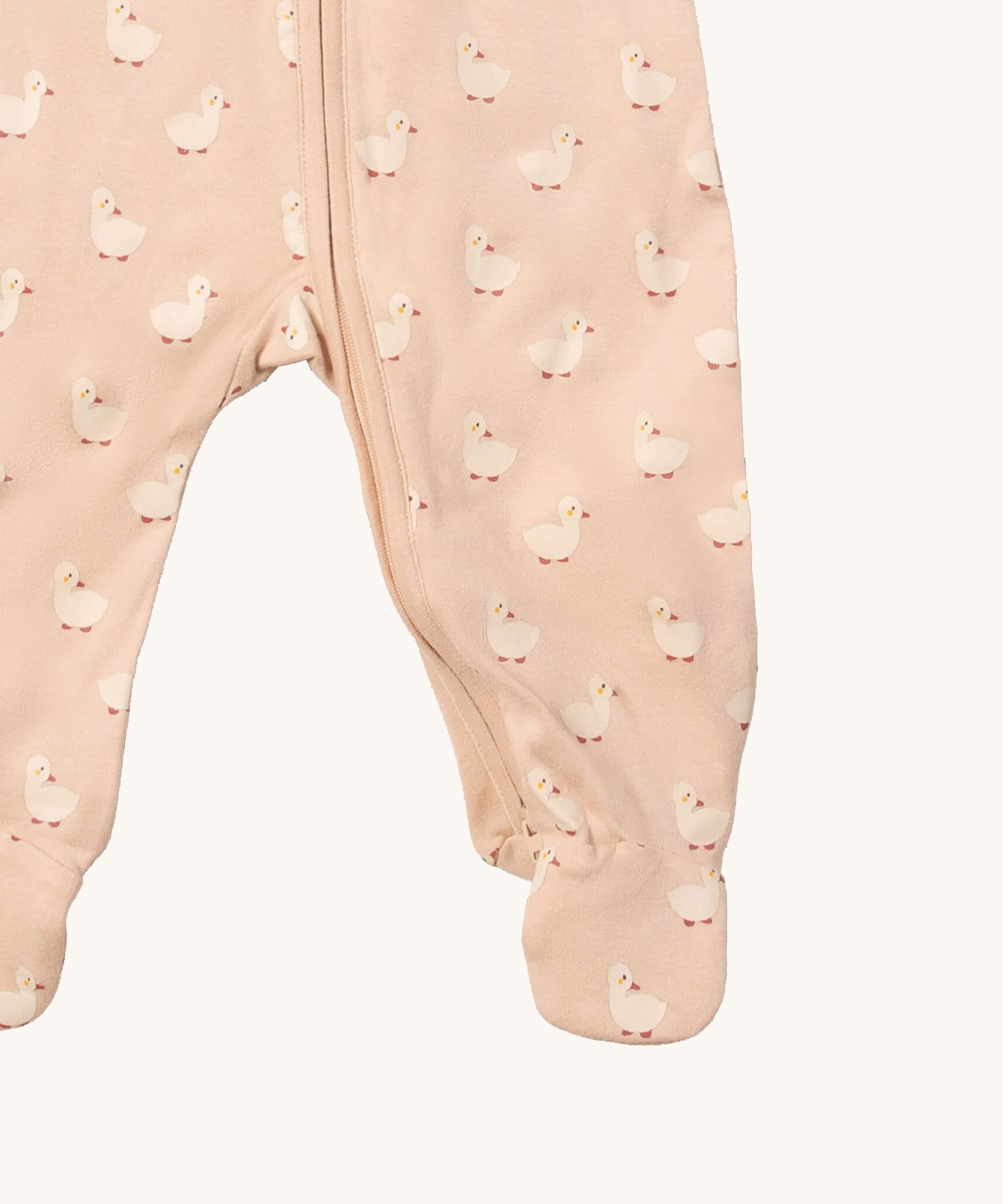 A close up of the Little Green Radicals turquoise rainbow baby grow, showing the zip detail around the crotch on light pink organic cotton fabric with cute duck prints.