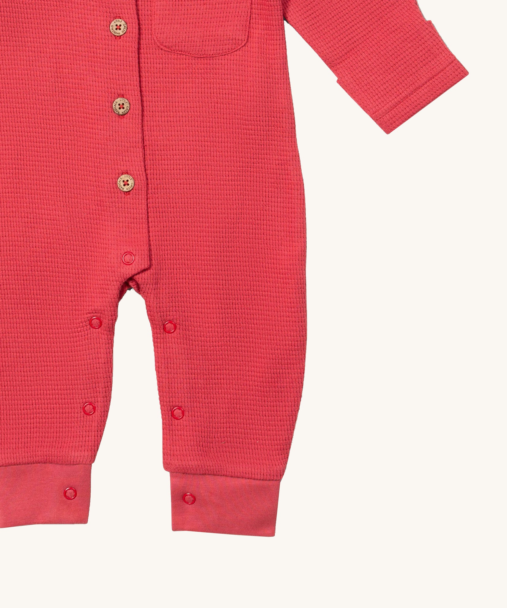 A close up of the Little Green Radicals pink waffle playsuit showing the button fastener detail and poppers around the crotch.