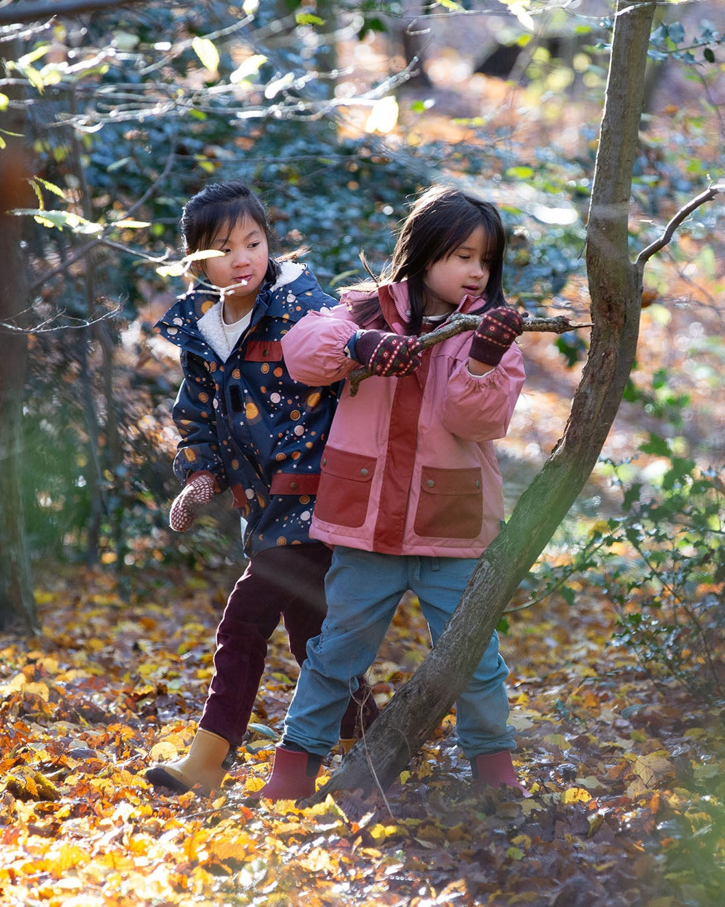 Two children playing in a forest with autumn leaves on the ground.