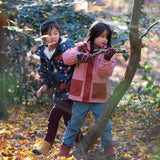 Two children playing in a forest with autumn leaves on the ground.