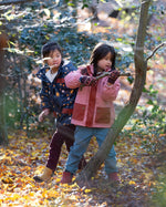 Two children playing in a forest with autumn leaves on the ground.
