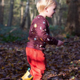 A child walking in woodland and wearing the Little Green Radicals flying birds quilted sweatshirt that's available at Babipur. A quilted style sweatshirt with cute prints of birds flying through a starry night on dark maroon organic cotton fabric.