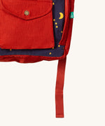 A close up of the Little Green Radicals ready for adventure backpack in dark night. Showing the front red pocket detail which features a button fastener on navy corduroy cotton fabric.