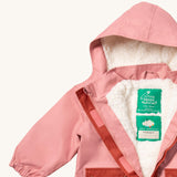 A close up of the Little Green Radicals waterproof coat in coral Showing the hood detail with sherpa fleece liner and name patch detail on blue recycled polyester fabric