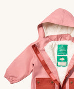 A close up of the Little Green Radicals waterproof coat in coral Showing the hood detail with sherpa fleece liner and name patch detail on blue recycled polyester fabric