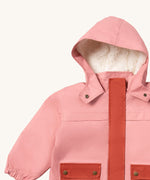 A close up of the Little Green Radicals waterproof coat in coral showing the sherpa fleece liner, the full length zip and 2 side pockets in dark pink trim detail on pink recycled polyester fabric