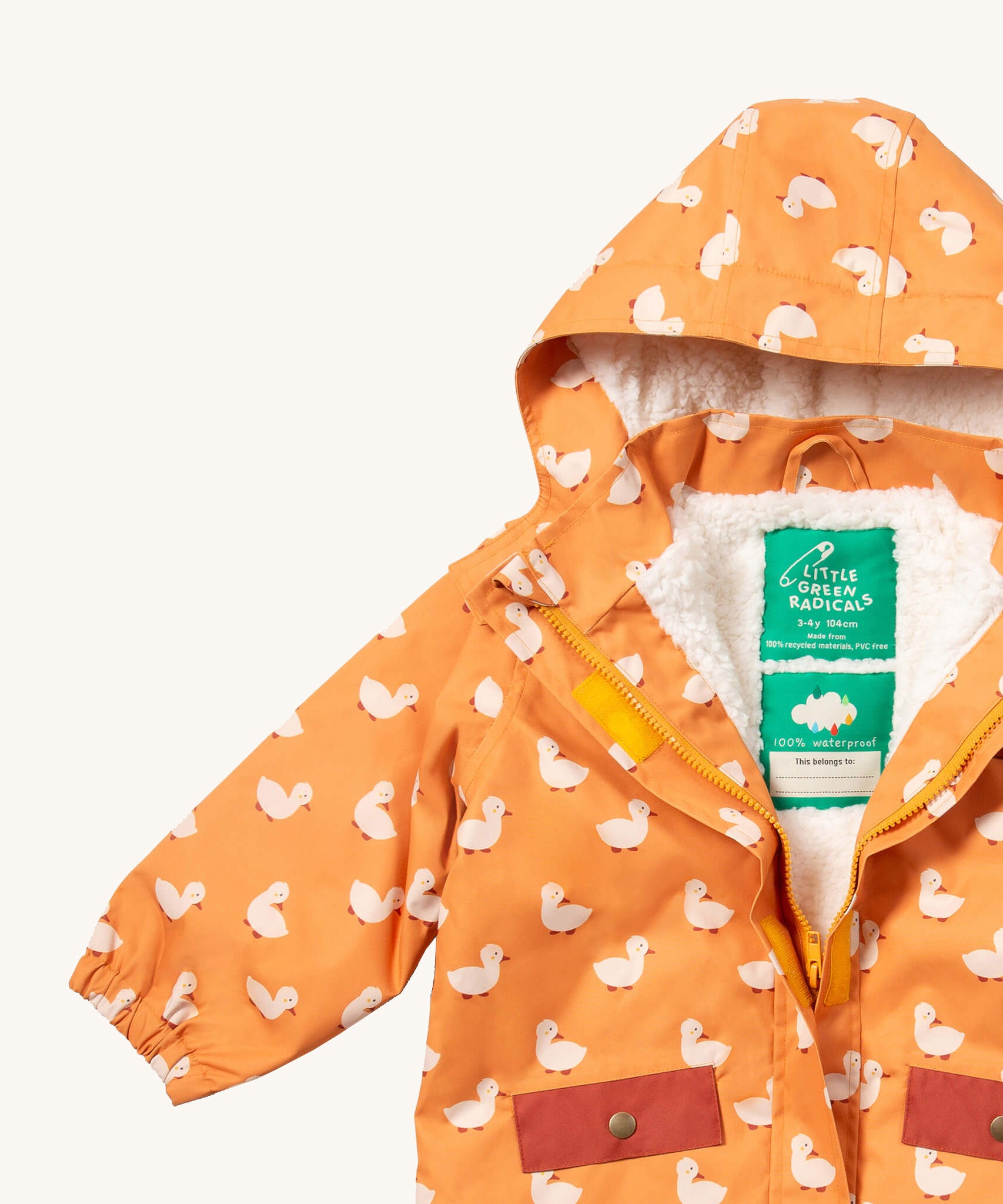 A close up of the Little Green Radicals waterproof coat in gold ducks showing the hood detail with sherpa fleece liner and name patch detail on yellow recycled polyester fabric