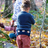 A child wearing the Little Green Radicals navy sheep snuggle knitted jumper outside showing the white speckles and cute sheep continuing around the jumper