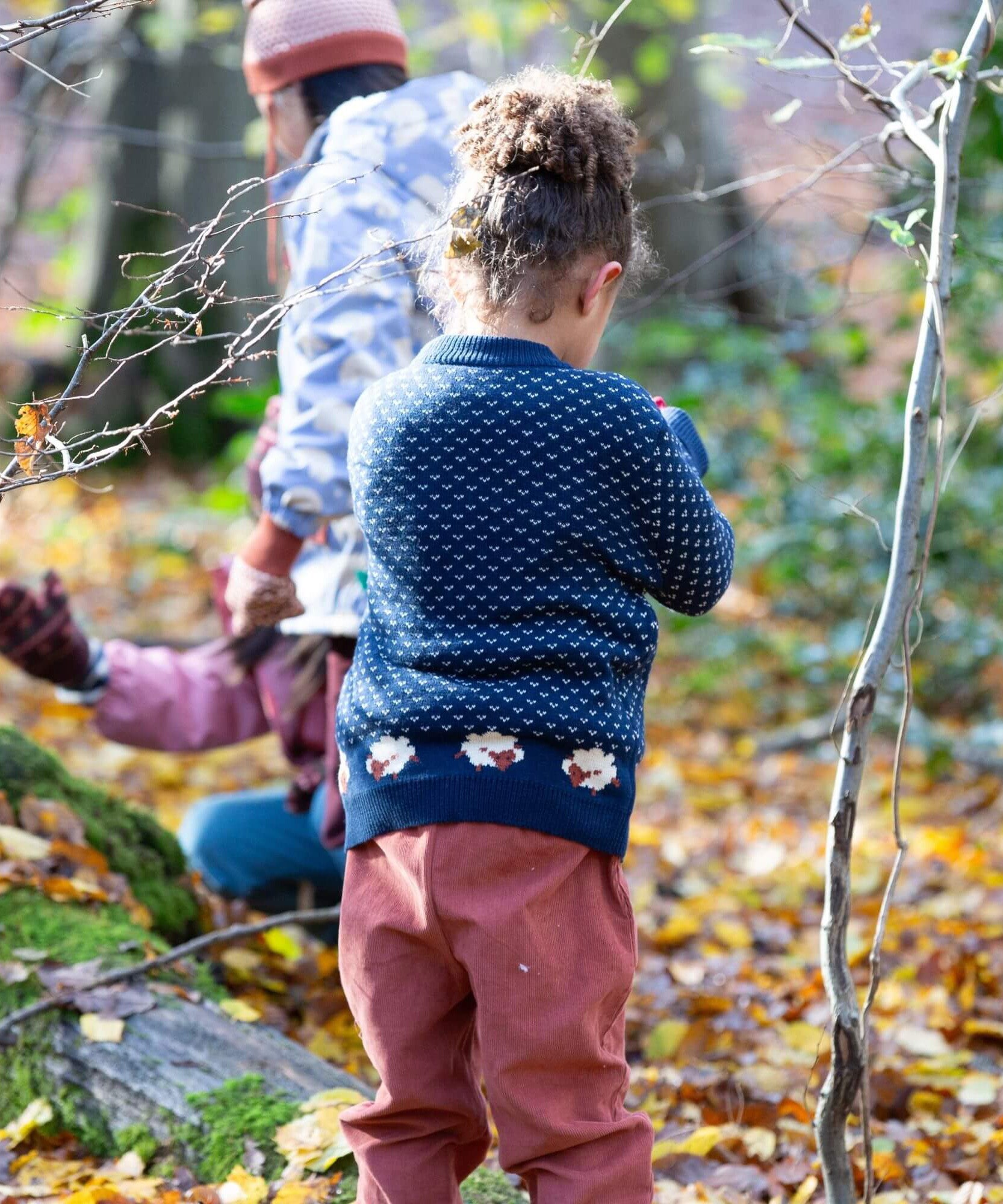 A child wearing the Little Green Radicals navy sheep snuggle knitted jumper outside showing the white speckles and cute sheep continuing around the jumper