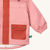 A close up of the Little Green Radicals waterproof coat in coral Showing the elasticated cuff detail and dark pink side pocket on pink recycled polyester fabric